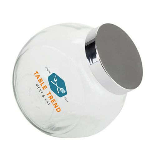 Bonbonglas mit silbernem Deckel und mehrfarbigem TableTrend-Logo auf der Vorderseite. Bonbonglas mit silbernem Deckel und mehrfarbigem TableTrend-Logo auf der Vorderseite.