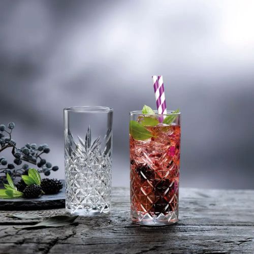 Gefülltes Timeless-Longdrink-Glas, attraktiv präsentiert im Innenraum mit Getränken.